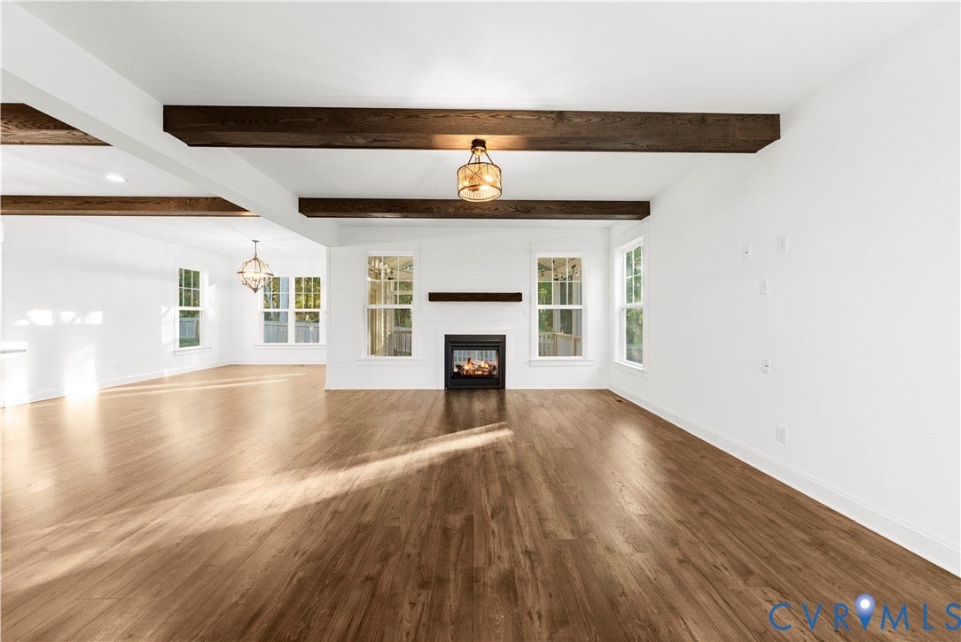 2613 Lilybank Place, NewMarket At RounTrey, Midlothian, VA 23112 Open-concept space featuring wood-finish flooring, exposed stained-wood ceiling beams, a central fireplace with a wood mantel, and multiple multi-pane windows