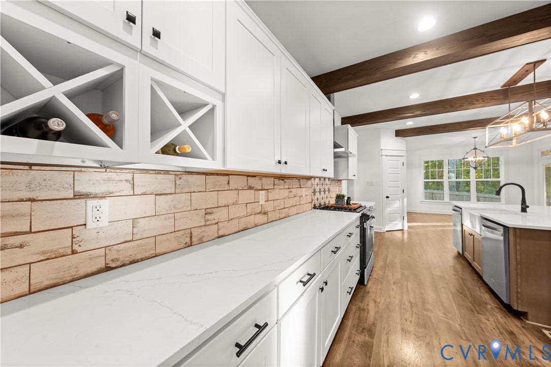 2613 Lilybank Place, NewMarket At RounTrey, Midlothian, VA 23112 Kitchen featuring white cabinetry with integrated wine storage, light-toned stone-style backsplash, wood-finish flooring, exposed ceiling beams, and a farmhouse-style sink