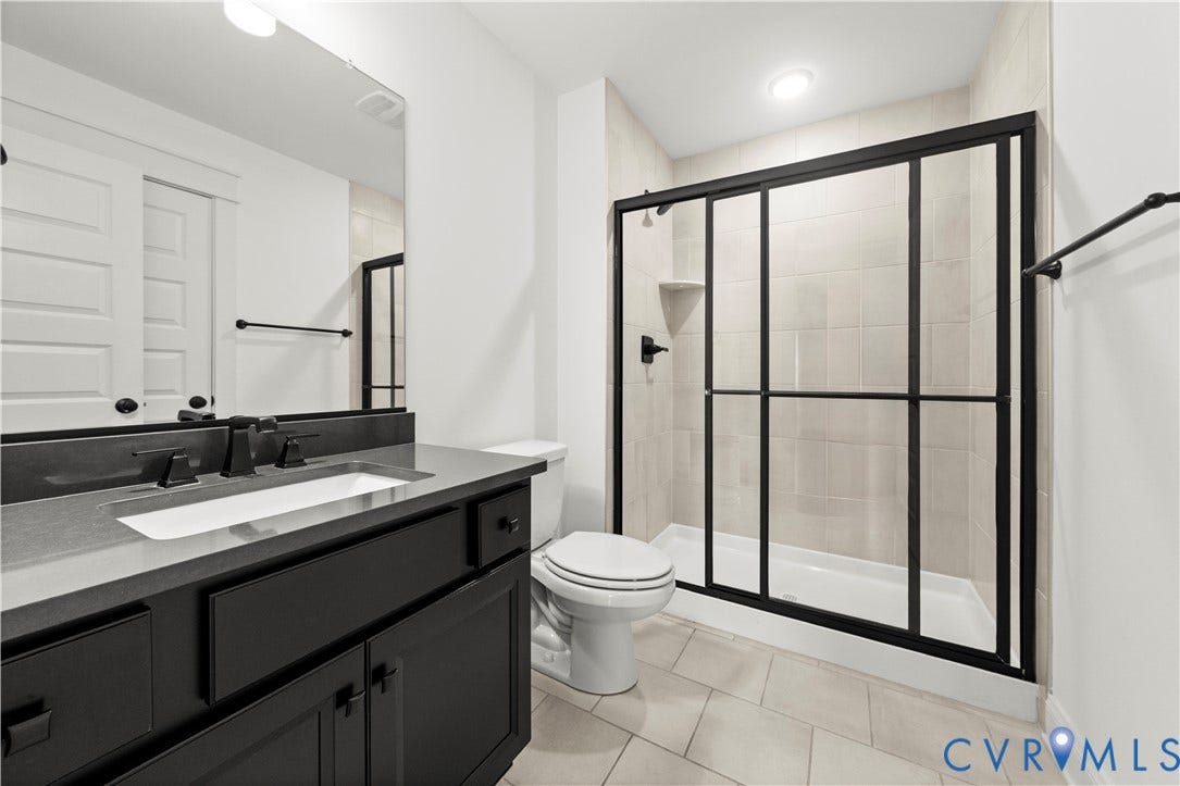 2613 Lilybank Place, NewMarket At RounTrey, Midlothian, VA 23112 Bathroom featuring a dark-finish vanity with a rectangular undermount sink, quartz countertop, walk-in shower with matte black sliding doors, and large-format tile flooring