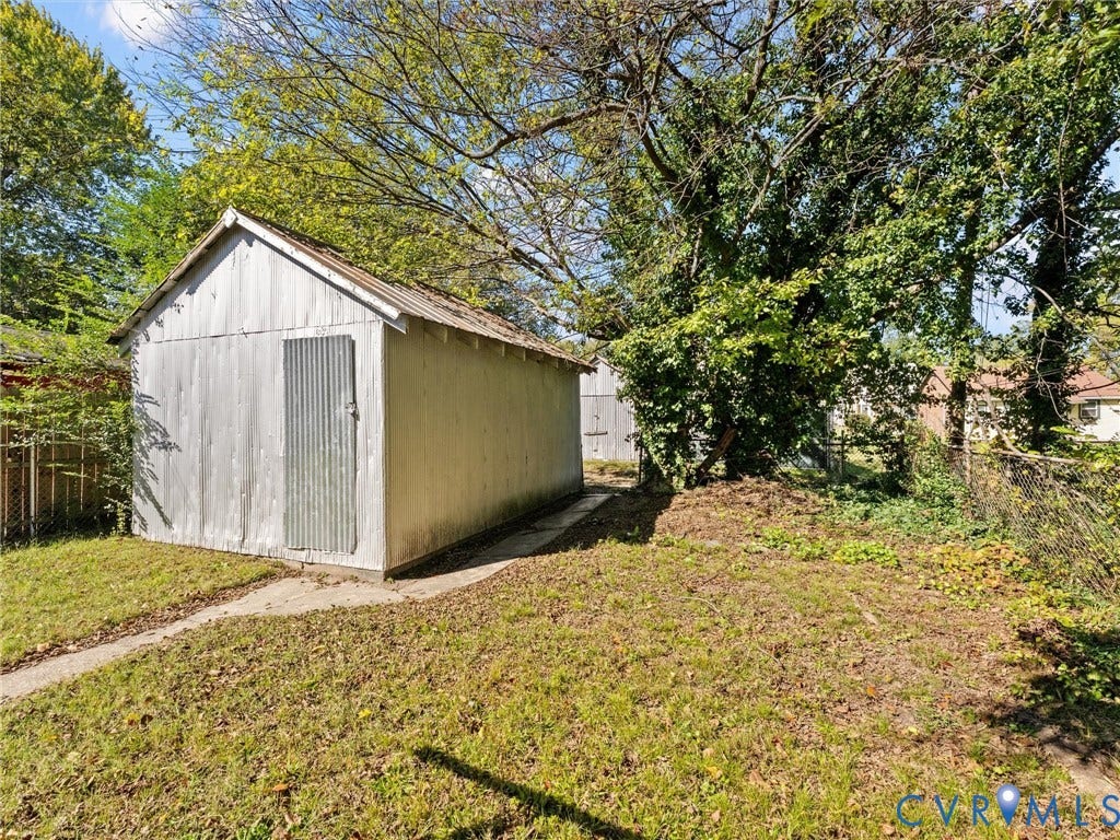 2305 Halifax Avenue, Oak Grove, Sandston, VA 23224 Detached metal storage structure with a corrugated finish, gable roof, and concrete pathway access on a lot with mature trees and chain-link fencing
