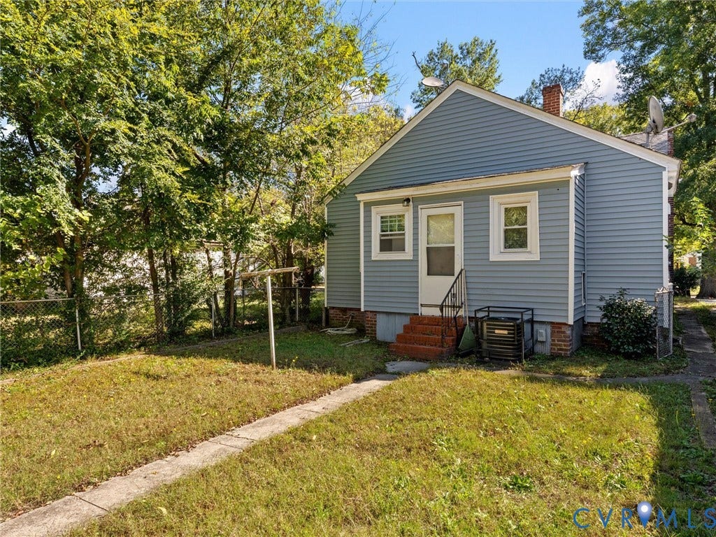 2305 Halifax Avenue, Oak Grove, Sandston, VA 23224 Rear exterior featuring blue horizontal siding, brick foundation elements, concrete walkway, and chain-link fencing