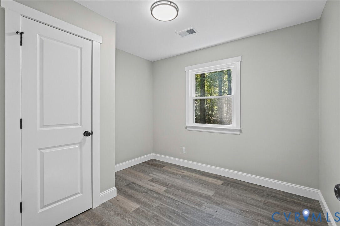 15227 Horseshoe Bridge Road, Hanover, VA 23047 Room interior featuring wood-finish flooring, crisp neutral wall paint, a single-hung window with casing, and a paneled interior door with matte black hardware