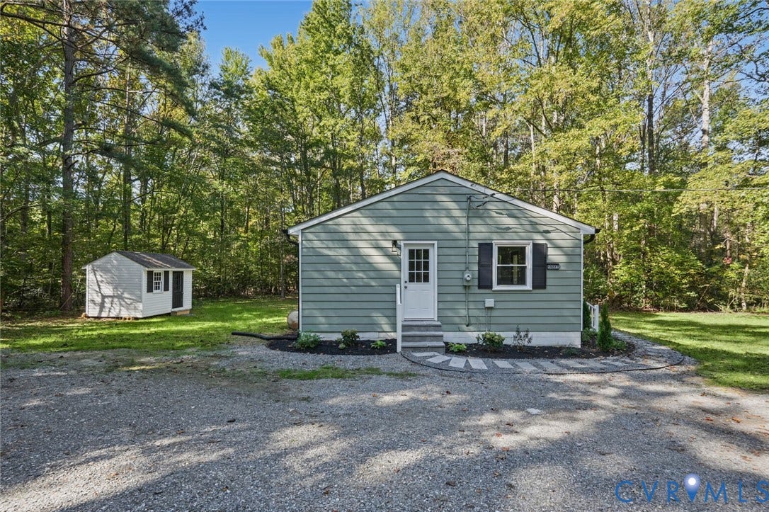 15227 Horseshoe Bridge Road, Hanover, VA 23047 Exterior featuring light-tone horizontal siding, dark shutters, a white entry door with glass paneling, a gravel driveway, and a detached storage structure