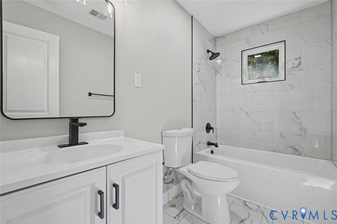 15227 Horseshoe Bridge Road, Hanover, VA 23047 Bathroom featuring a white vanity cabinet, rectangular mirror with a black frame, matte black hardware, and a tub enclosure with large-format light-toned patterned wall tiling