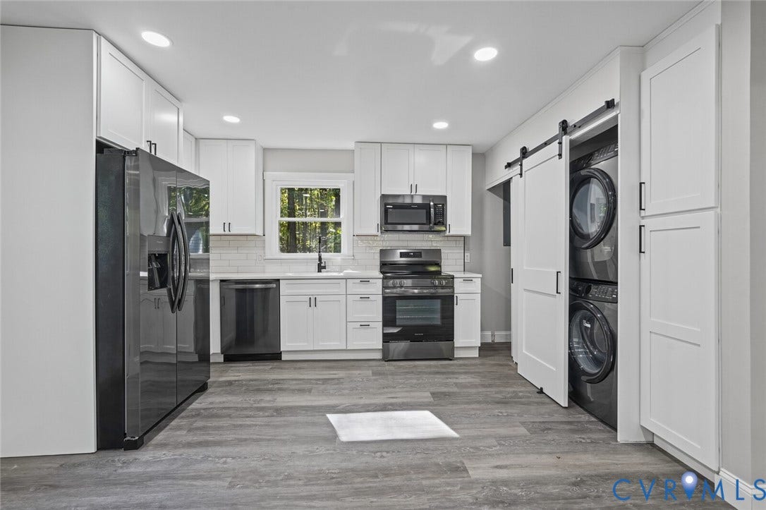 15227 Horseshoe Bridge Road, Hanover, VA 23047 Kitchen featuring white shaker-style cabinetry, wood-finish flooring, a white subway tile backsplash, dark stainless steel appliances, and a sliding barn door concealing the laundry area
