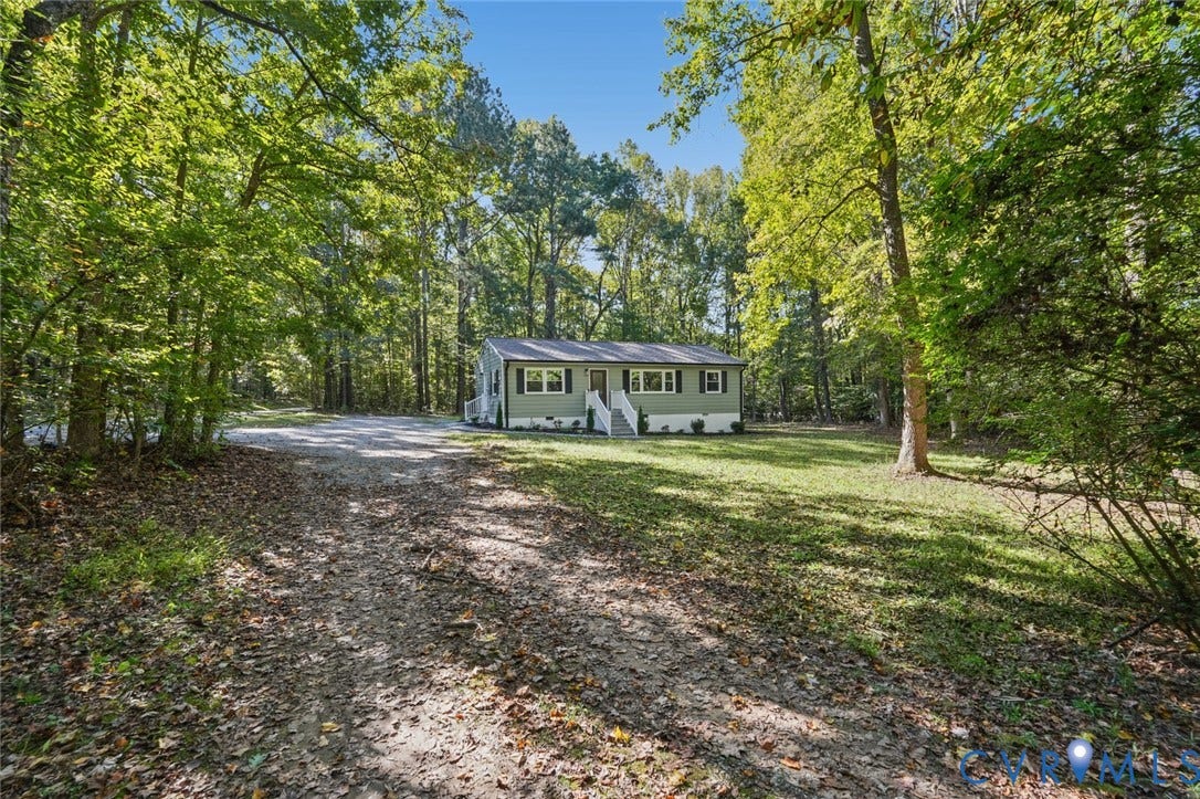 15227 Horseshoe Bridge Road, Hanover, VA 23047 Single-story home featuring a light green exterior, white-railed front steps, shingle roof, dark shutters, and a gravel driveway situated on a wooded lot