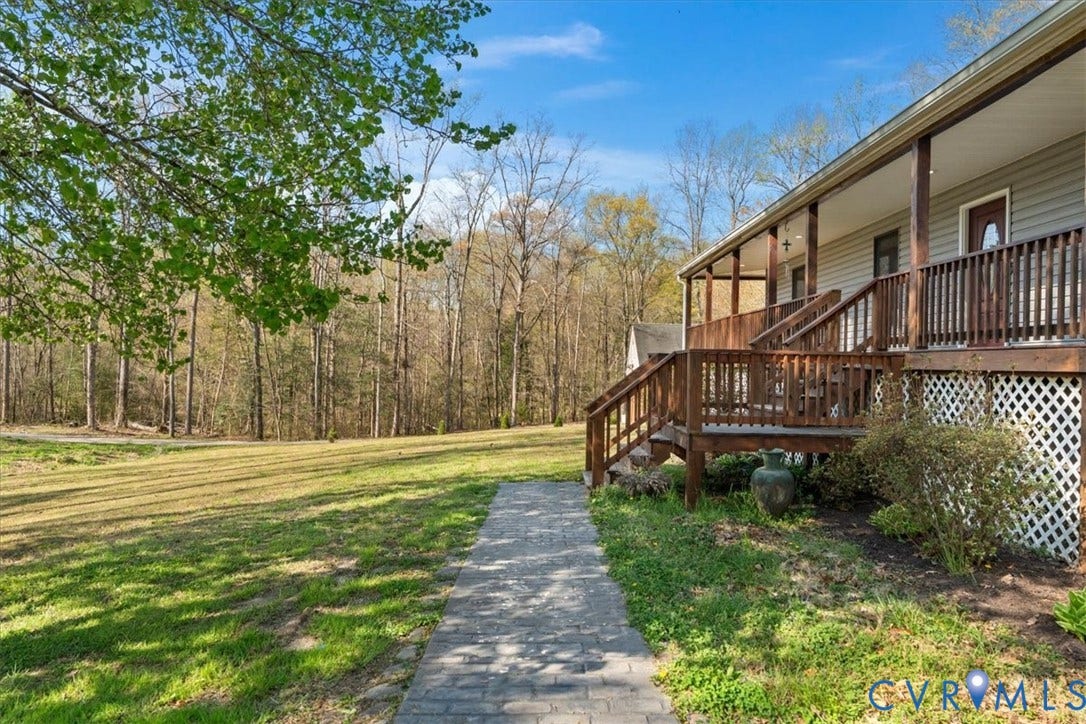 7040 Old Roxbury Road, Average, New Kent, VA 23141 Expansive lawn featuring mature trees, a paver walkway, and a raised wooden deck with lattice skirting