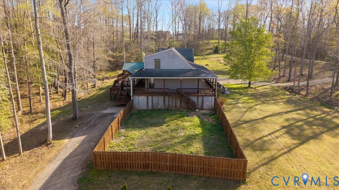 7040 Old Roxbury Road, Average, New Kent, VA 23141 Multi-level exterior featuring a covered wrap-around deck, fenced yard area, and a gravel driveway, situated on a wooded lot