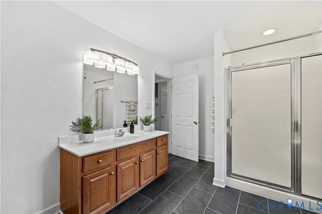 7040 Old Roxbury Road, Average, New Kent, VA 23141 Bathroom featuring a wood-finish vanity with a stone countertop, an integrated sink, a multi-bulb light fixture above a large mirror, and a shower with sliding glass doors over dark tile flooring