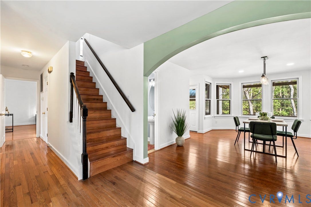 7040 Old Roxbury Road, Average, New Kent, VA 23141 Open-concept interior featuring wood-finish flooring, a staircase with a black handrail and wood treads, an arched entryway, and multiple double-hung windows