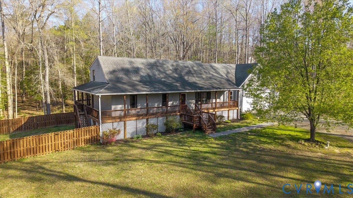 7040 Old Roxbury Road, Average, New Kent, VA 23141 Two-story residence featuring grey siding, an elevated wrap-around wood deck, lattice skirting, a wood privacy fence, and a wooded lot