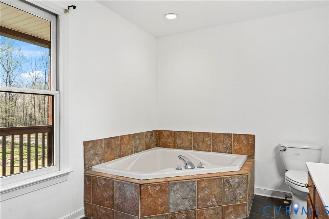 7040 Old Roxbury Road, Average, New Kent, VA 23141 Corner soaking tub featuring a tile surround, chrome faucet fixtures, and a dual-pane window