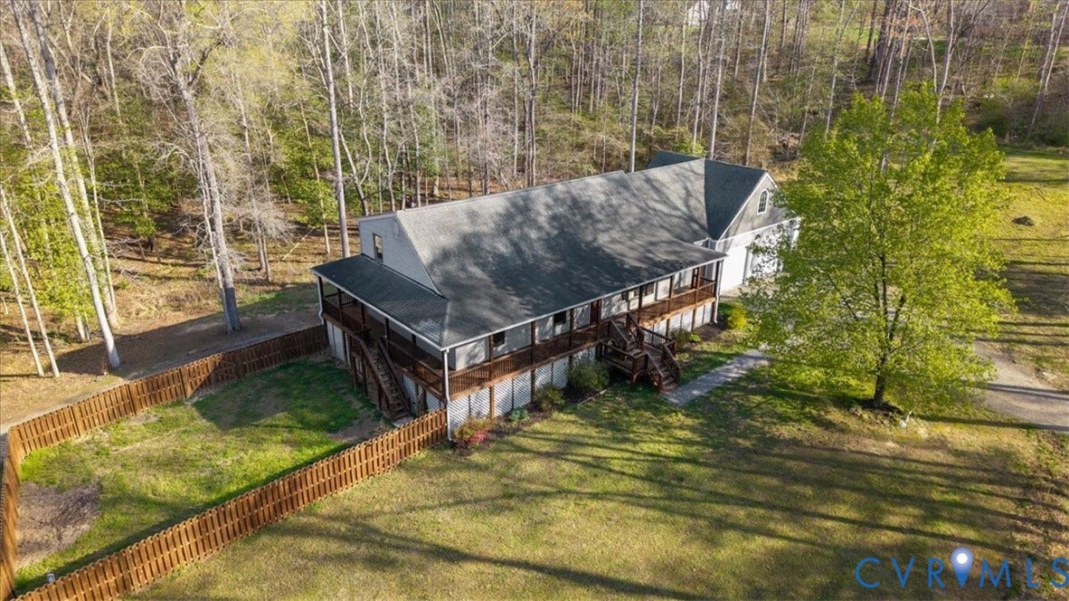 7040 Old Roxbury Road, Average, New Kent, VA 23141 Multi-level residence featuring a wrap-around wooden deck, shingle roof, attached garage, and a fenced-in yard, bordered by mature woodland