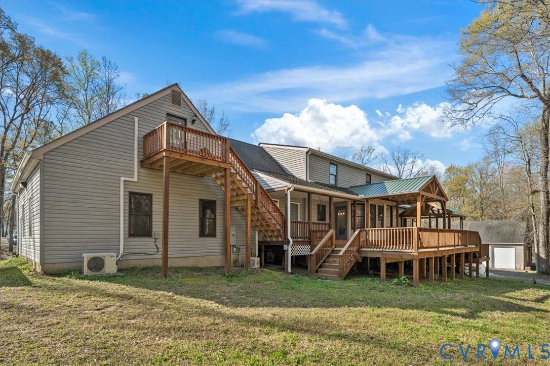 7040 Old Roxbury Road, Average, New Kent, VA 23141 Multi-level exterior featuring light gray horizontal siding, a wrap-around wooden deck, a secondary-level balcony with stairs, and a metal-roofed covered patio area