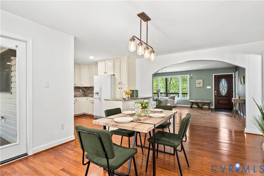7040 Old Roxbury Road, Average, New Kent, VA 23141 Dining area featuring wood-finish flooring, a linear four-light pendant fixture, white cabinetry, a stone-surround backsplash, and a prominent architectural archway