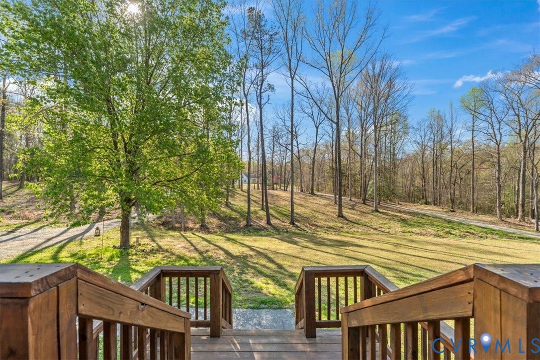 7040 Old Roxbury Road, Average, New Kent, VA 23141 Elevated wood deck featuring vertical balusters and a wide staircase, overlooking a expansive grass lot with mature trees