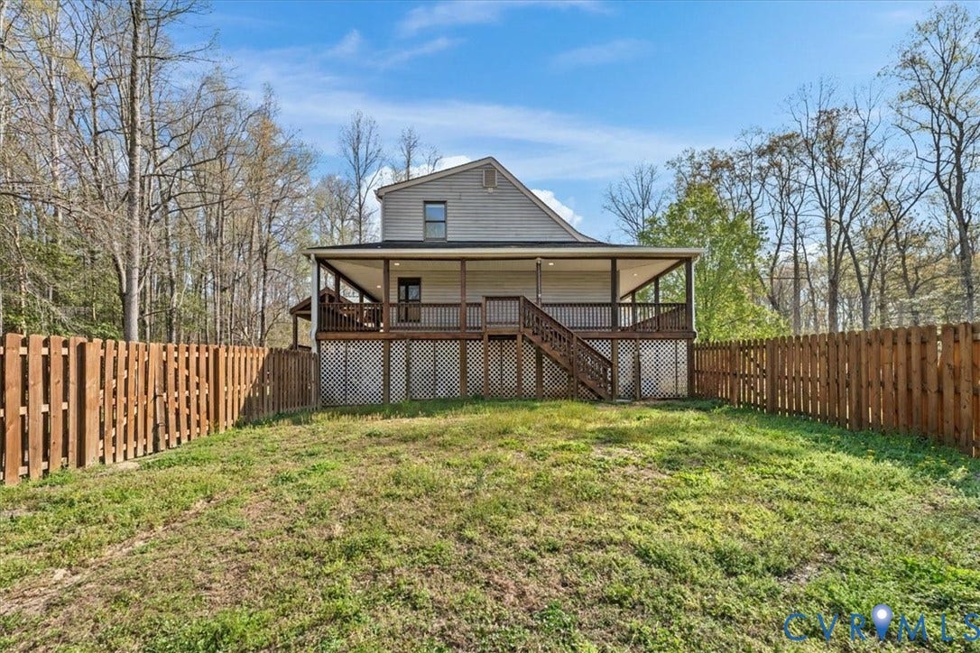 7040 Old Roxbury Road, Average, New Kent, VA 23141 Exterior featuring a full-width covered deck with wooden railing and lattice skirting, enclosed by a wood privacy fence on a lot bordered by mature trees