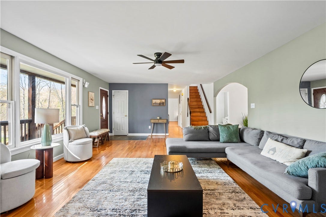 7040 Old Roxbury Road, Average, New Kent, VA 23141 Living area featuring polished wood-finish flooring, an arched entryway, natural wood-tone staircase, ceiling fan, and large windows