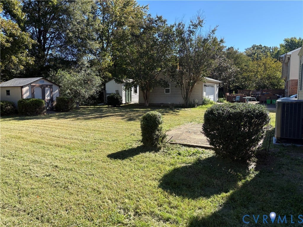 1708 Shewalt Drive, Fairfield, VA 23228 Expansive backyard featuring a manicured lawn, concrete patio area, two detached storage structures, and mature trees