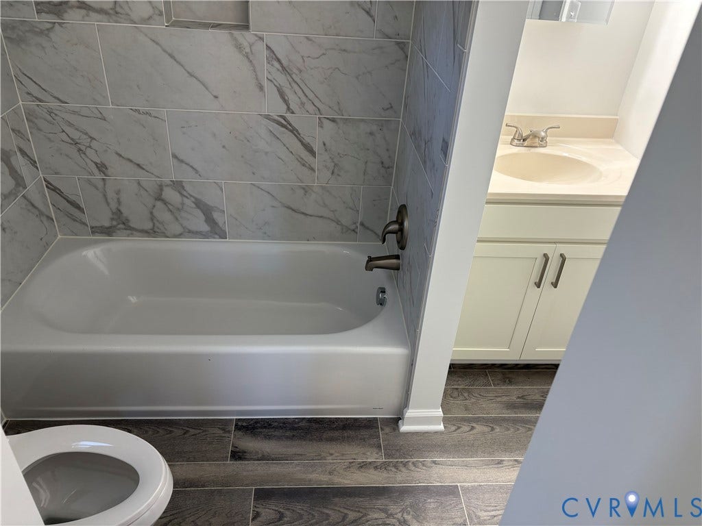 1708 Shewalt Drive, Fairfield, VA 23228 Bathroom 3rd level featuring a tub-shower combination with floor-to-ceiling large-format stone-patterned tile, wood-finish flooring, white cabinetry with metallic hardware, and an integrated countertop sink