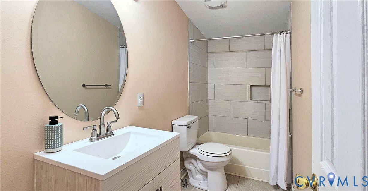 24110 Genito Road, Amelia, VA 23002 Vanity with a solid surface countertop, integrated sink, and metallic faucet, complemented by an oval wall-mounted mirror, ceramic tile shower surround with a built-in recessed niche, and tile flooring
