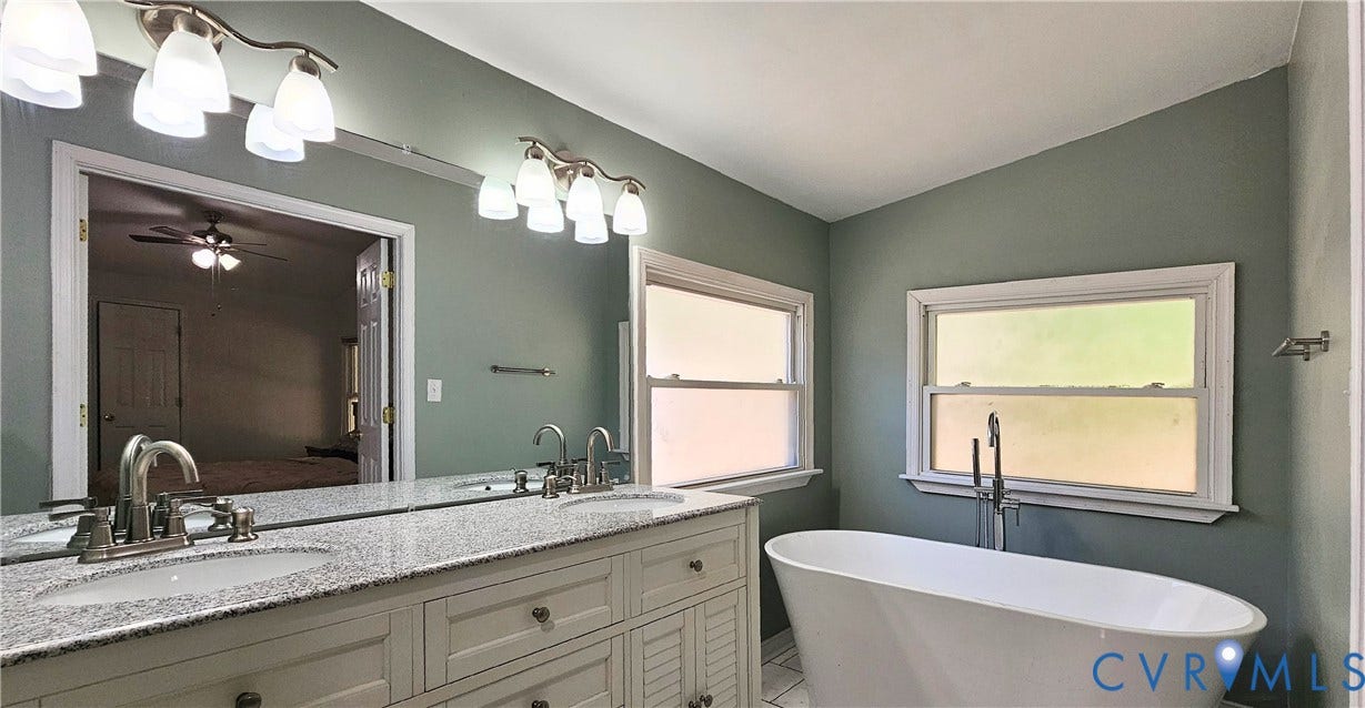 24110 Genito Road, Amelia, VA 23002 Double vanity with stone-finish countertop, undermount sinks, freestanding soaking tub, dual wall-mounted light fixtures, and large plate glass mirror