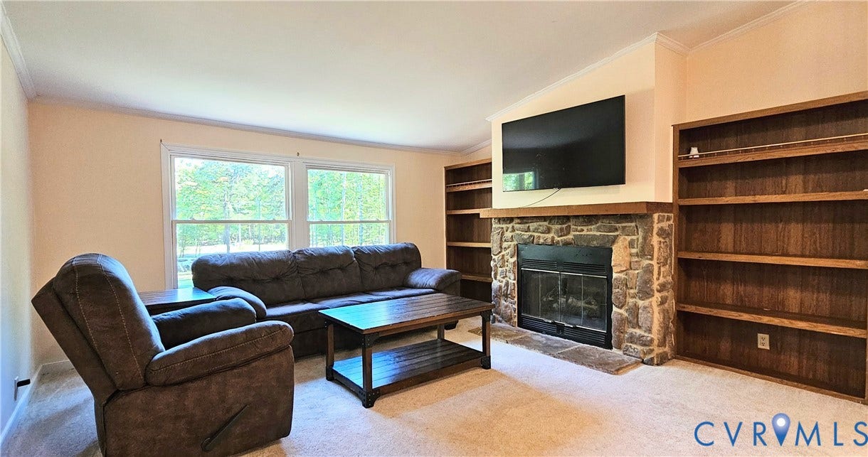 24110 Genito Road, Amelia, VA 23002 Living area featuring a floor-to-ceiling stone fireplace, wood-finish built-in shelving, and large double-pane windows
