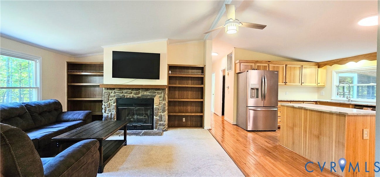 24110 Genito Road, Amelia, VA 23002 Open concept living area featuring a stone fireplace with integrated built-in shelving, hardwood flooring, wooden cabinetry, and a ceiling fan