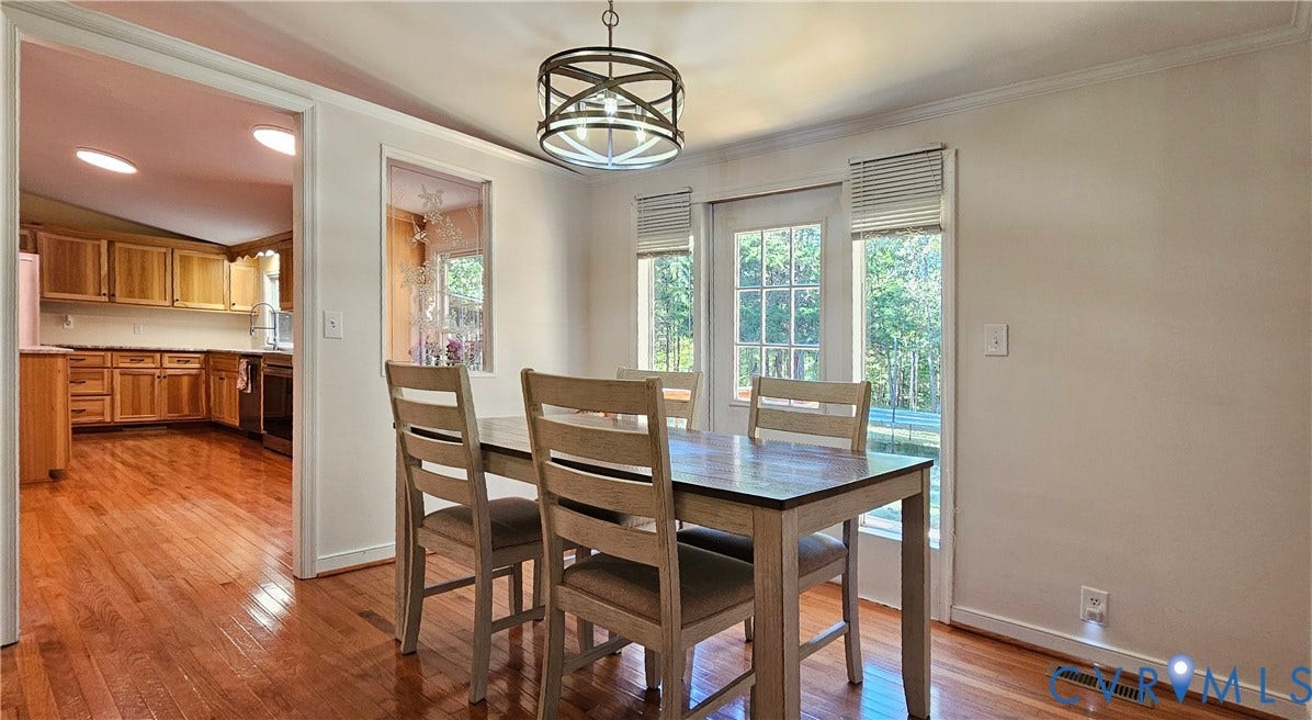 24110 Genito Road, Amelia, VA 23002 Dining area featuring wood-finish flooring, a drum-style chandelier, a pass-through wall window, and a glass-paned door providing outdoor visibility