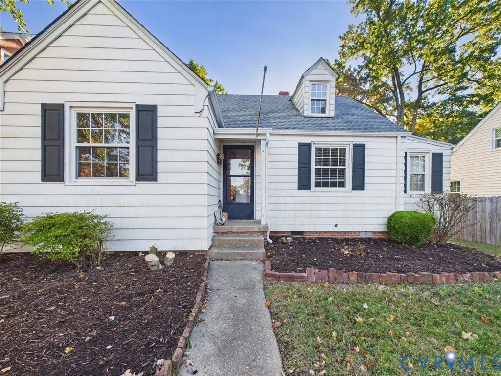 6902 Three Chopt Road, Richmond, VA 23226 Cape Cod exterior featuring white horizontal siding, dark decorative shutters, a gabled dormer window, and a concrete walkway bordered by brick edging