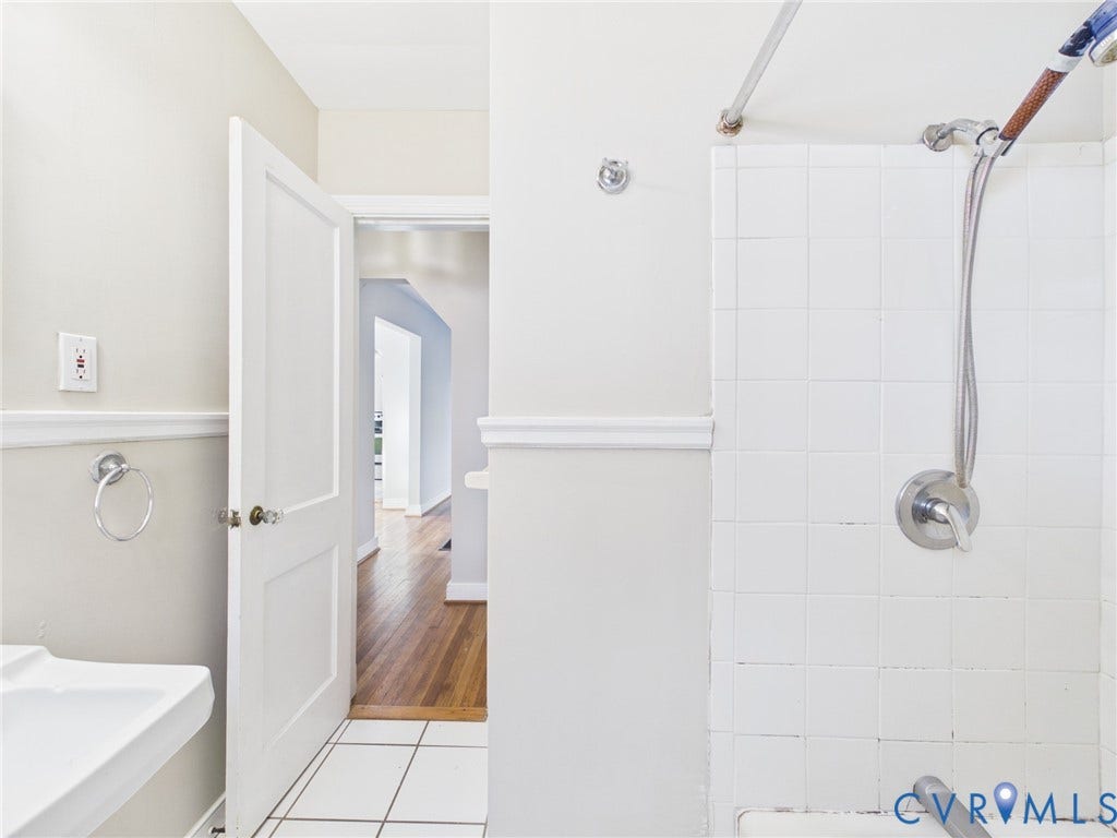 6902 Three Chopt Road, Richmond, VA 23226 Wall-mounted hand shower fixture, white ceramic wall tiling, pedestal sink, chair rail molding, and wood-finish flooring