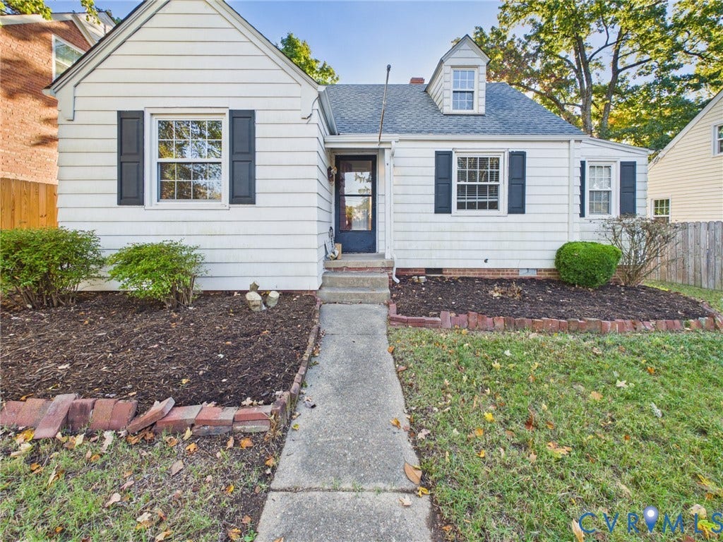 6902 Three Chopt Road, Richmond, VA 23226 Cape Cod exterior featuring white horizontal siding, dark window shutters, a gabled roofline with a dormer, and brick-edged garden beds