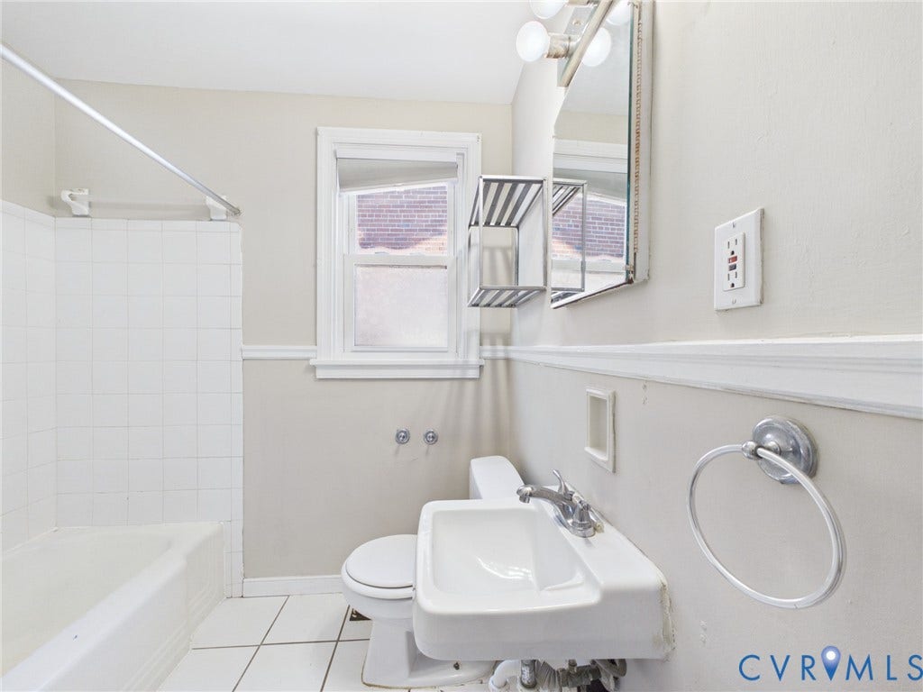 6902 Three Chopt Road, Richmond, VA 23226 Bathroom featuring a white porcelain wall-mounted sink with a metallic faucet, white tile floor, tub with a tiled surround, and wall-mounted vanity mirror with integrated lighting
