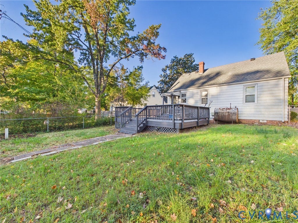 6902 Three Chopt Road, Richmond, VA 23226 Rear exterior featuring a raised wooden deck with lattice skirting, light-colored siding, a brick chimney, and mature trees