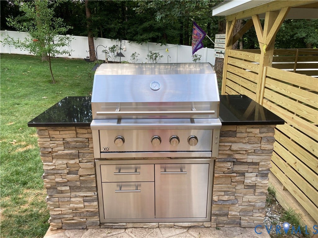1120 Black Heath Road, Robious/Huguenot, Midlothian, VA 23113 Outdoor kitchen island featuring an XO stainless steel gas grill, granite countertop, stacked stone base, and integrated stainless steel storage space.