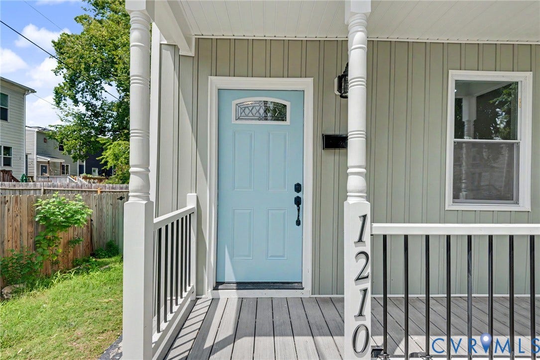 1210 N 24th Street, Church Hill Central, Richmond, VA 23223 Covered front porch featuring board-and-batten siding, a light blue entry door with decorative glass inlay, turned porch columns, and a black metal railing