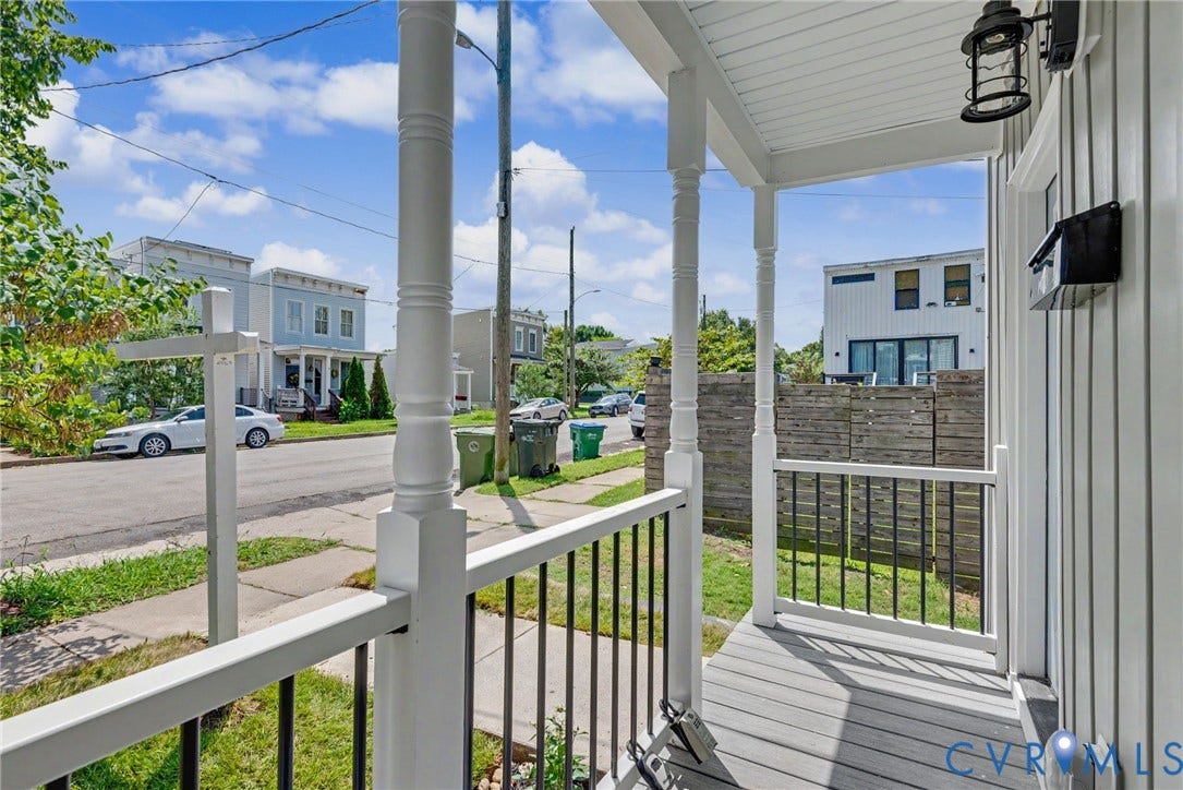 1210 N 24th Street, Church Hill Central, Richmond, VA 23223 Covered front porch featuring white structural columns, black metal railings, wood-finish flooring, and a wall-mounted exterior light fixture