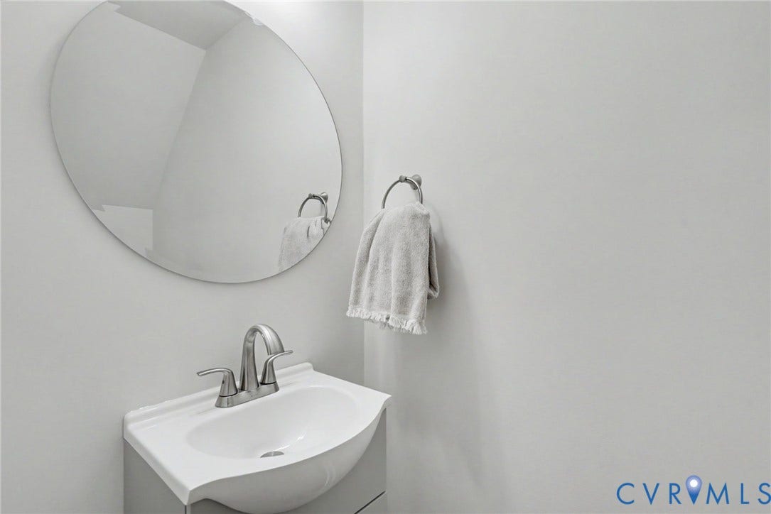 1210 N 24th Street, Church Hill Central, Richmond, VA 23223 Wall-mounted oval mirror above a vanity with an integrated basin, brushed-metal centerset faucet, and circular towel ring