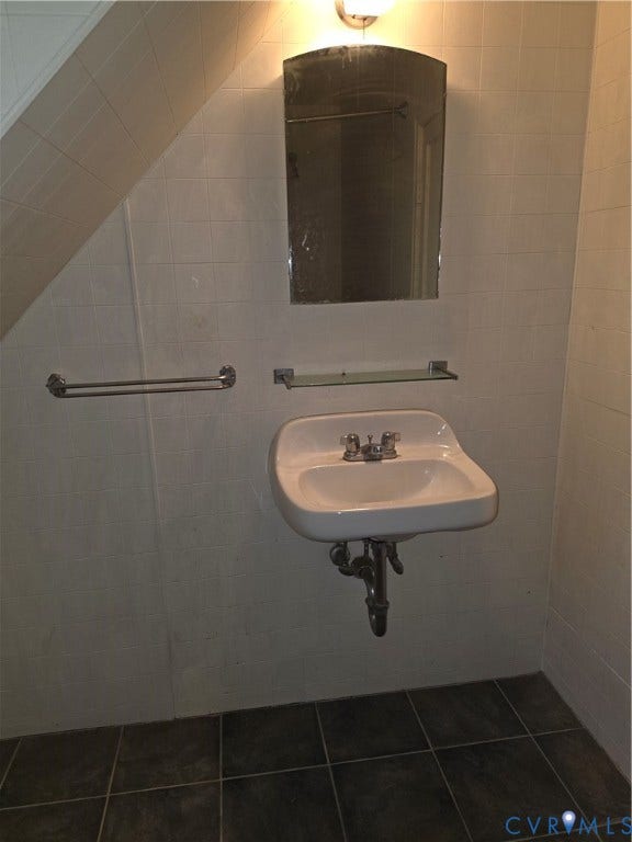 4114 Crestwood Road, Established, Richmond, VA 23227 Wall-mounted porcelain sink with chrome fixtures, glass shelf, arched mirror, and tiled wall surfacing, complemented by dark ceramic floor tiling