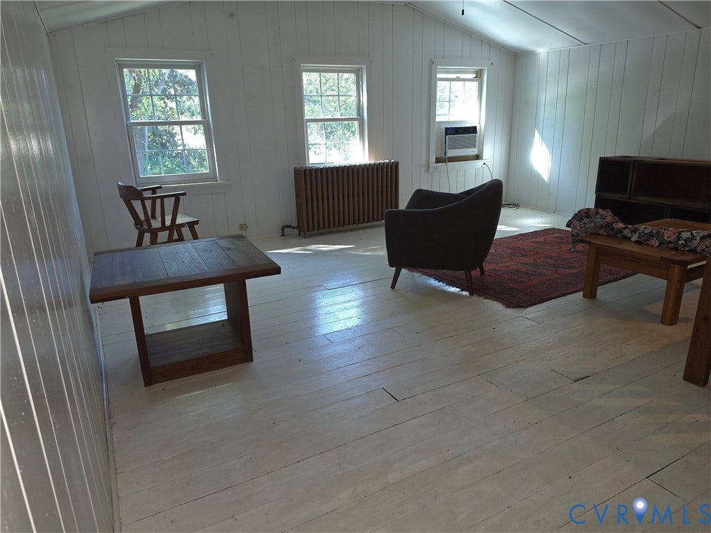 4114 Crestwood Road, Established, Richmond, VA 23227 Interior room featuring white-painted vertical plank wall paneling, painted wood-finish flooring, three double-hung windows, and a classic metal radiator
