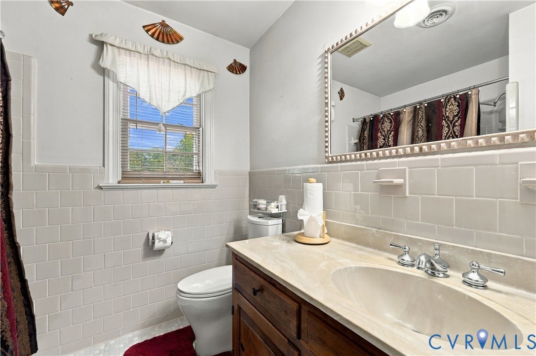 8307 Wallingford Lane, Chickahominy Bluffs, Henrico, VA 23227 Bathroom featuring a wood-finish vanity with a light-toned countertop, integrated oval basin, large framed mirror, and cream-colored wall tile