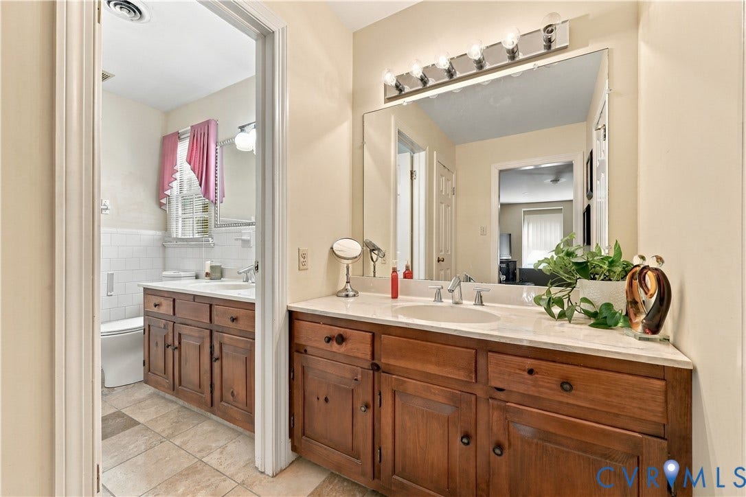8307 Wallingford Lane, Chickahominy Bluffs, Henrico, VA 23227 Bathroom featuring wood-finish cabinetry, neutral stone-finish countertops, undermount sinks, full-width vanity mirrors, and multi-bulb strip lighting