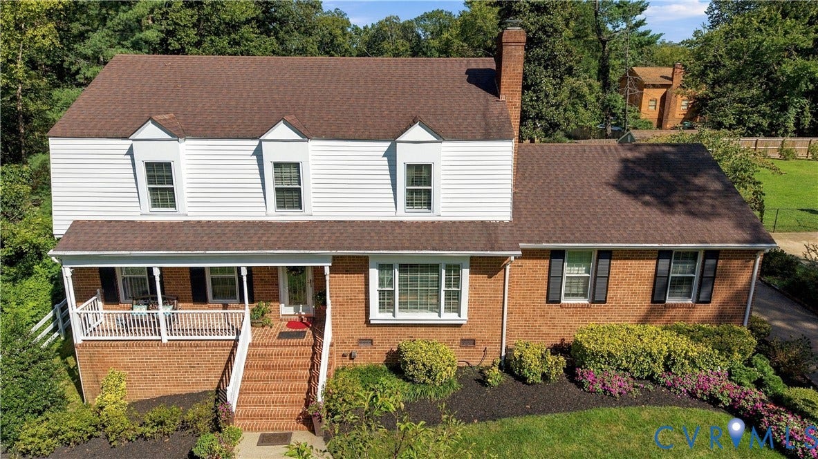 8307 Wallingford Lane, Chickahominy Bluffs, Henrico, VA 23227 Two-story residence featuring a combination of brick and horizontal siding, a covered front porch with white railing, brick exterior staircase, three dormer windows, and a prominent exterior brick chimney