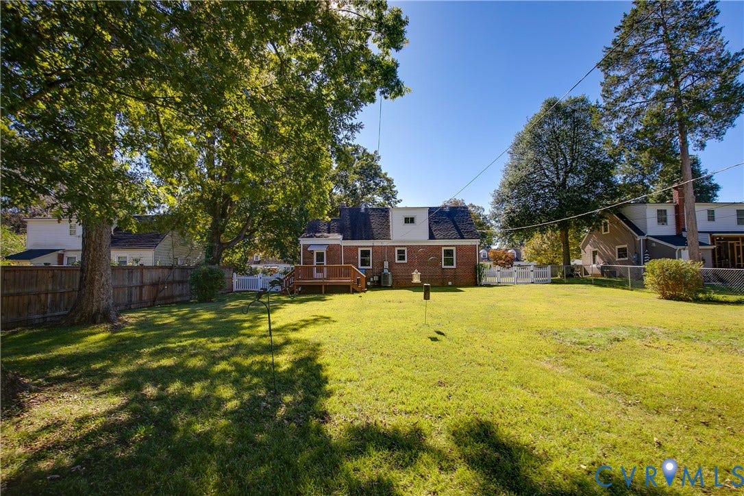 Brick exterior, elevated wooden deck, and expansive lawn area enclosed by wood fencing and white picket style fencing