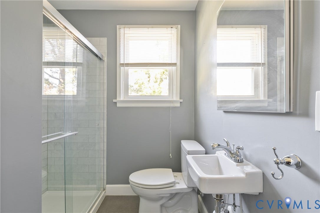 Bathroom featuring a glass-enclosed shower with tiled surround, wall-mounted sink with chrome faucet, and a frameless mirror