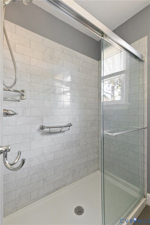 Walk-in shower featuring subway tile surround, sliding glass door, handheld shower head, and built-in metal shelving
