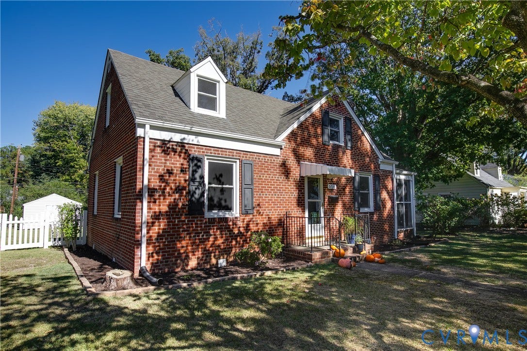 Red brick exterior featuring a steep-pitched roof, dual dormer windows, shutter-framed window casings, and a metal-awning front entry