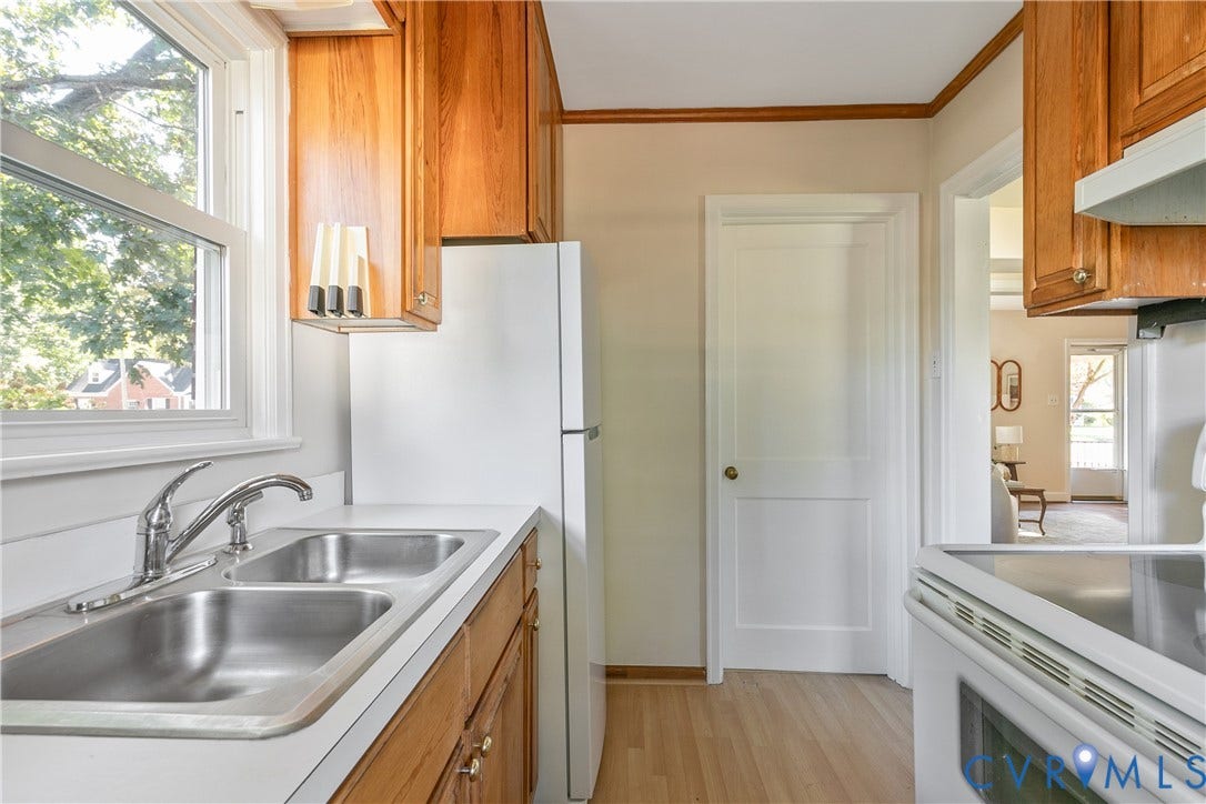 Kitchen featuring wood cabinetry, stainless steel double-basin sink, high-arc faucet, and wood-finish flooring