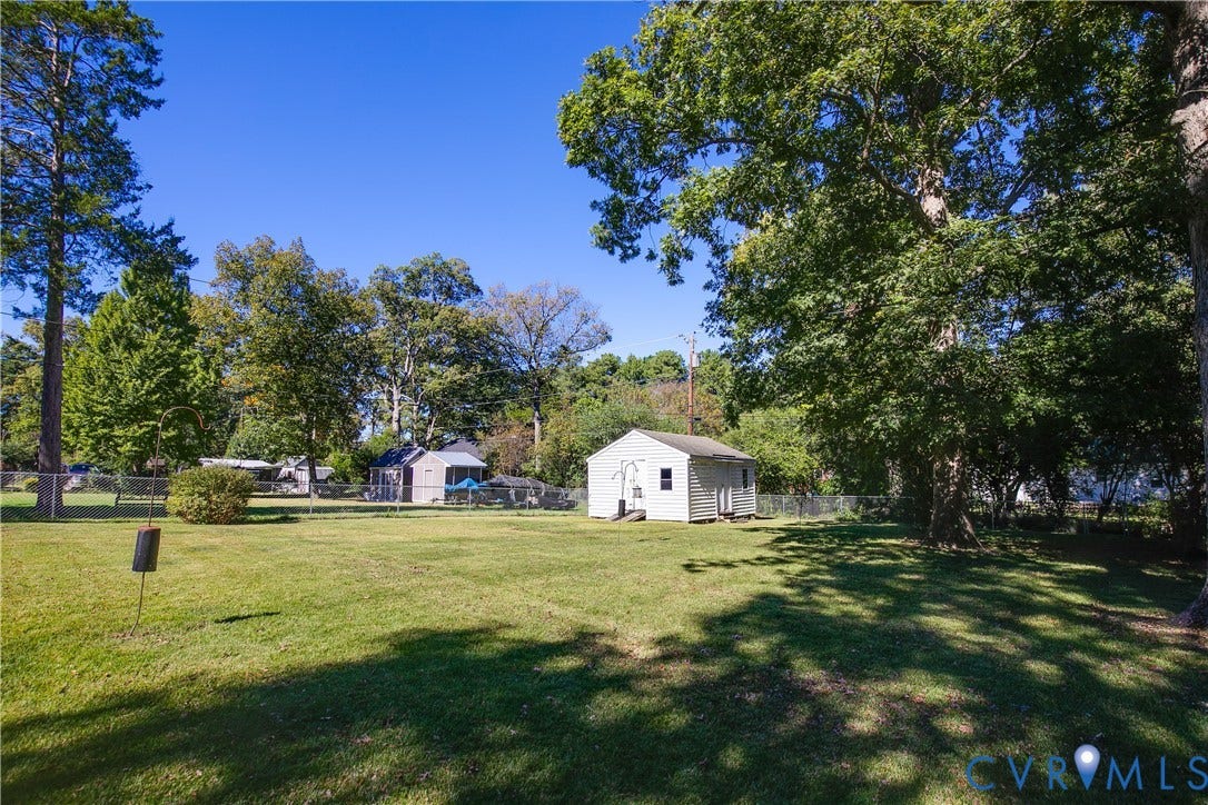 Expansive backyard featuring a large grass lawn, perimeter chain-link fencing, mature trees, and a detached white-siding storage structure