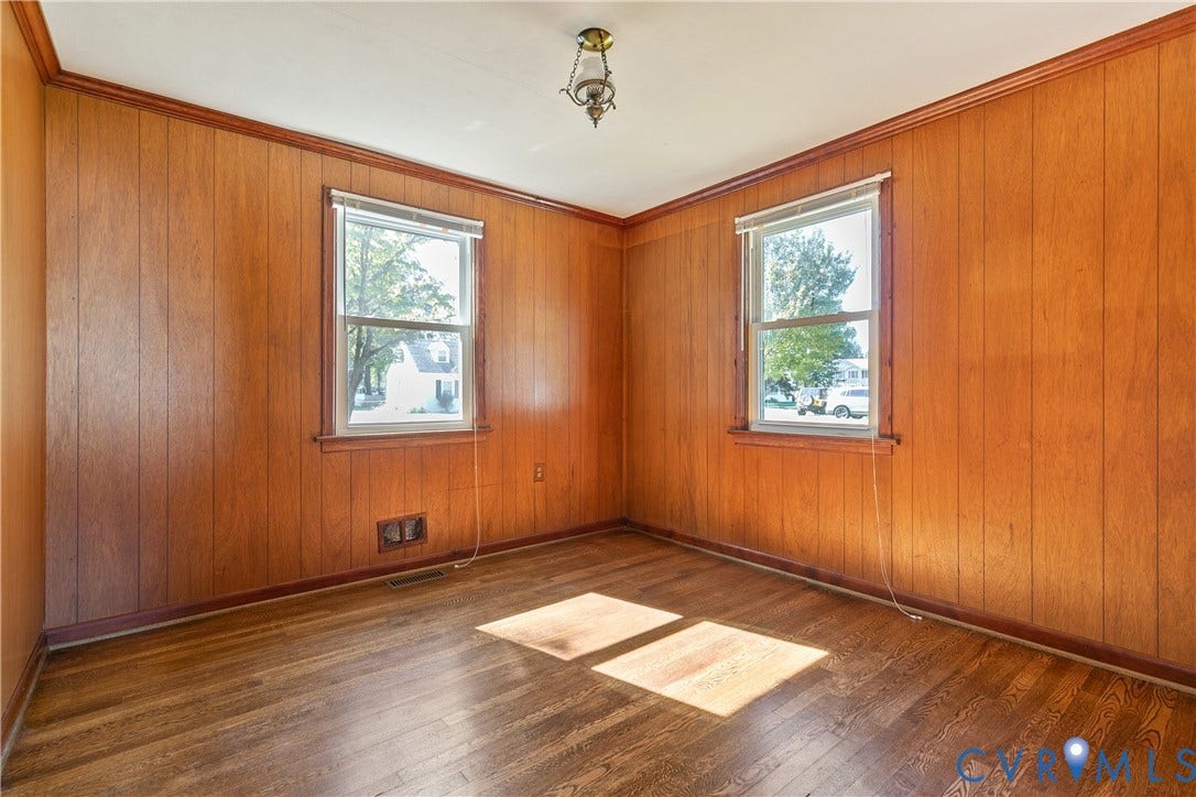 Wood-paneled walls with crown molding, wood-finish flooring, and two double-hung windows